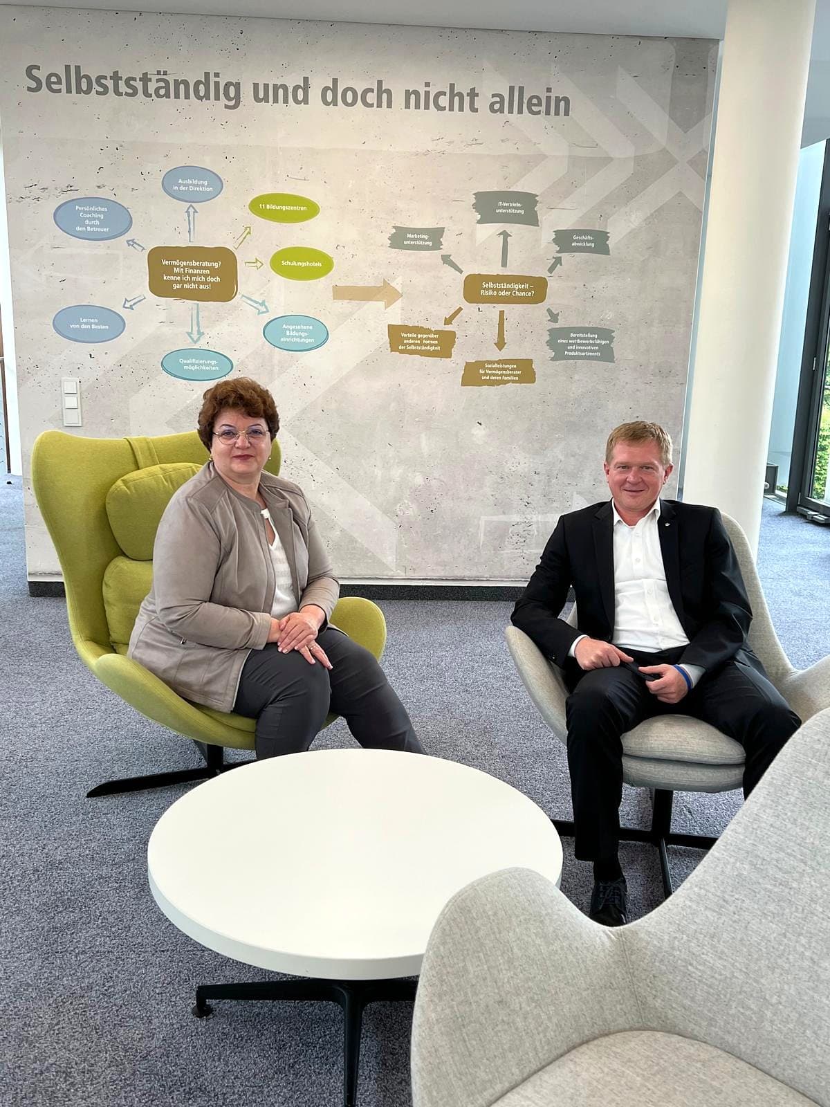 Larissa Etzel und ein Gesprächspartner sitzen in Sesseln vor einer Wand mit dem Leitsatz „Selbstständig und doch nicht allein“.