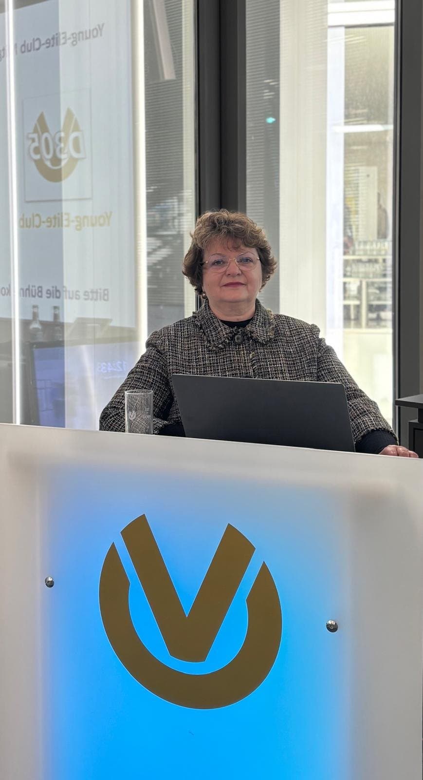 Larissa Etzel steht an einem Rednerpult mit dem Logo der Deutschen Vermögensberatung.