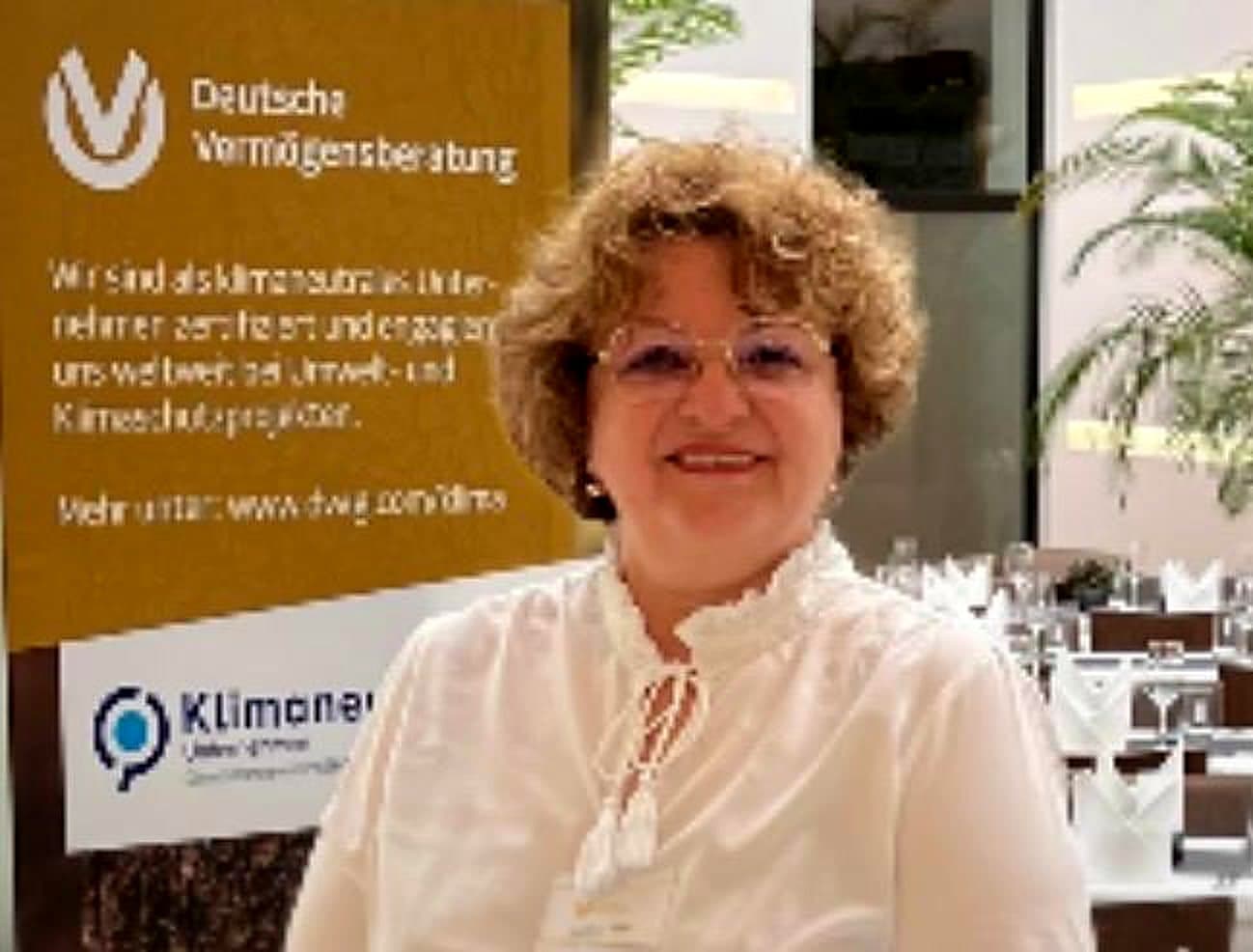 Larissa Etzel lächelt in die Kamera, hinter ihr ein Aufsteller der Deutschen Vermögensberatung.